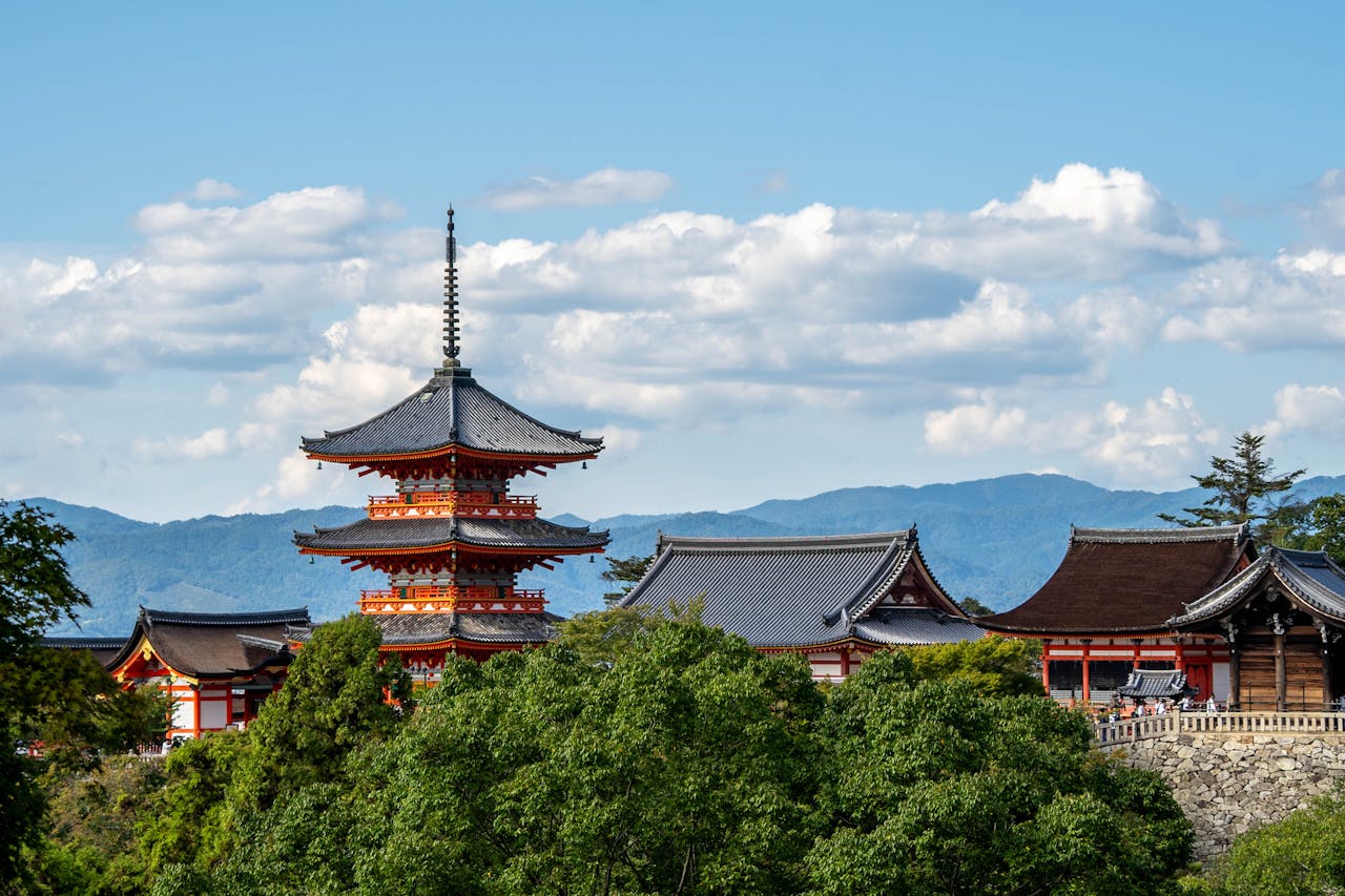View of Kiyomizu-dera Temple's pagoda amidst lush greenery with mountains in Kyoto, Japan.